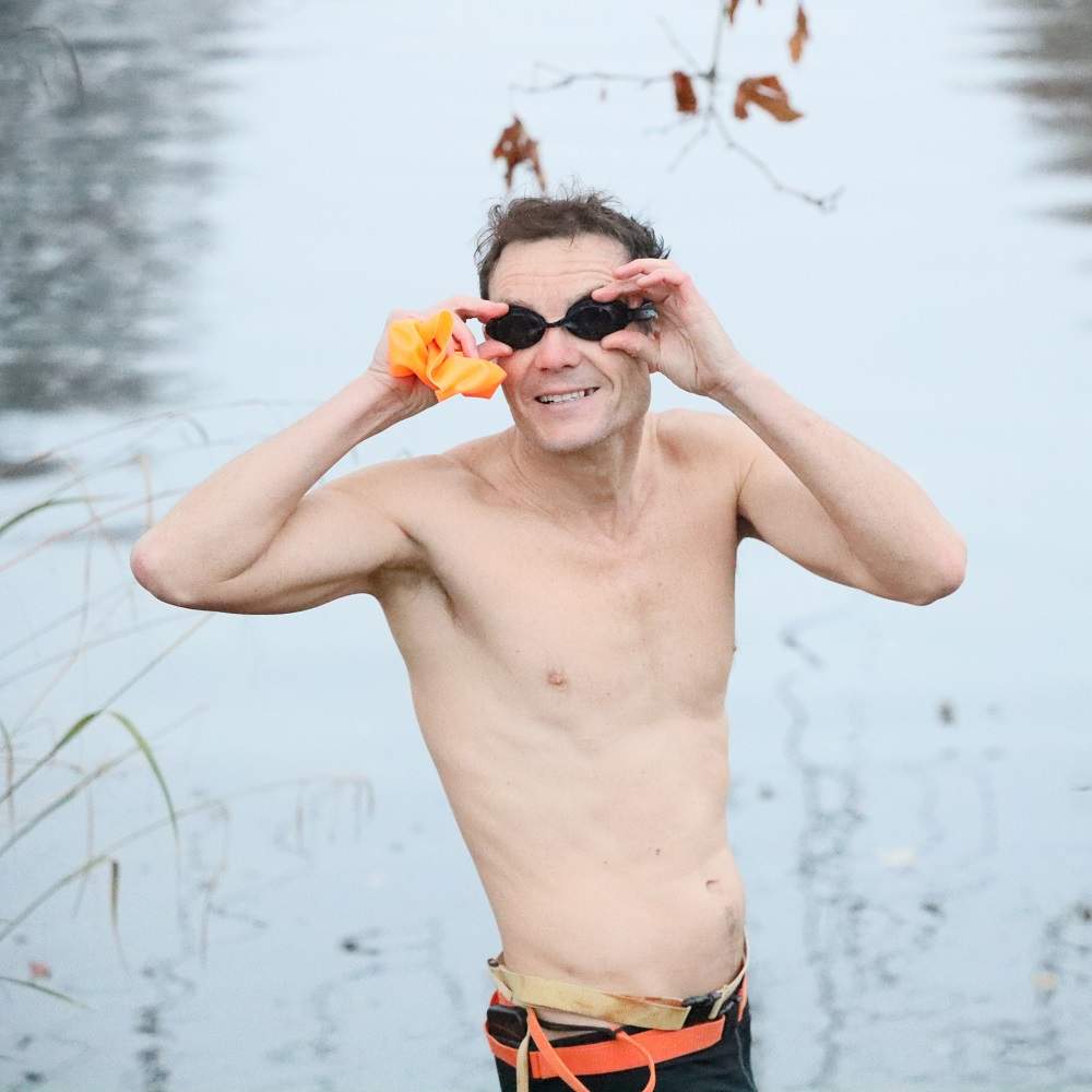 A swimmer adjusting their goggles while standing in front of a river