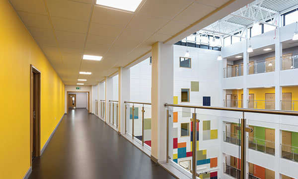 An image of a school corridor with a yellow wall with doorways to classrooms on one side.