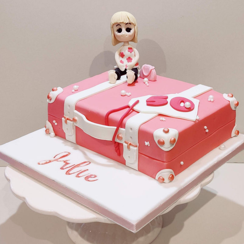 A pink suitcase modelled cake with character topper for a special birthday.